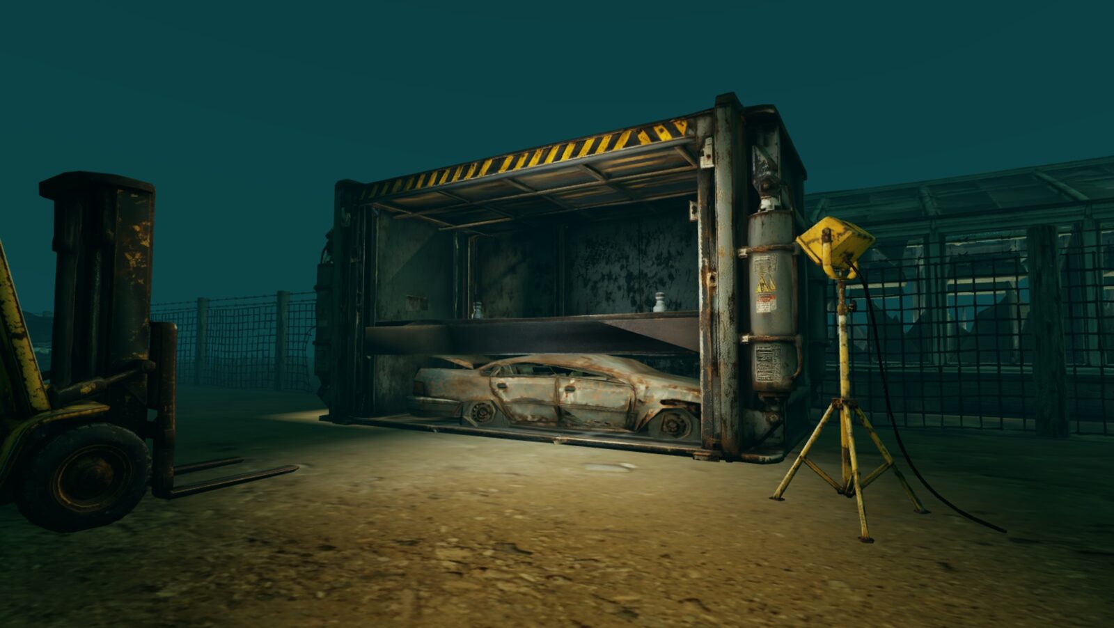 The car crusher with a wrecked car inside, a forklift and a work light beside it